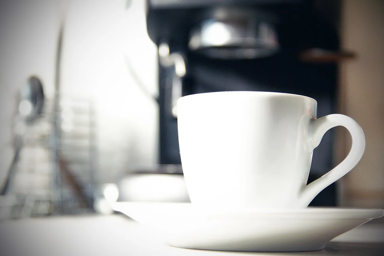 Real coffee cup and saucer with a coffee machine in the background